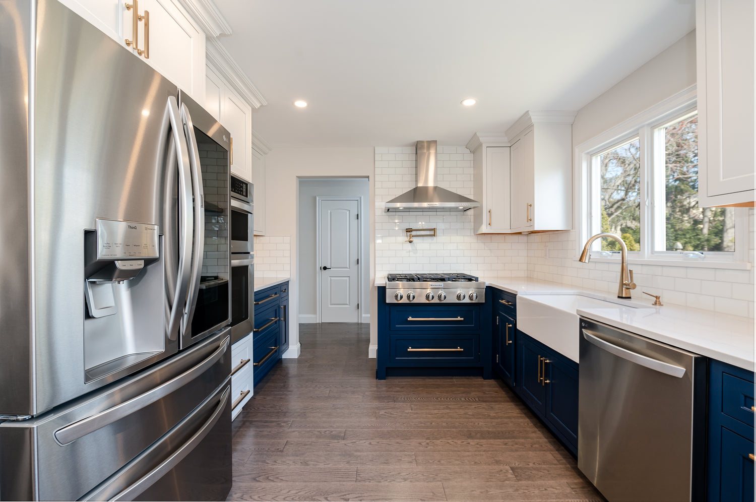 "After" Photo of Kitchen Renovation HOMEREDI did in Port Washington, NY.  White and Blue Shaker Galley Kitchen with Farmhouse sink, Cambria Quartz countertops and gold accents.