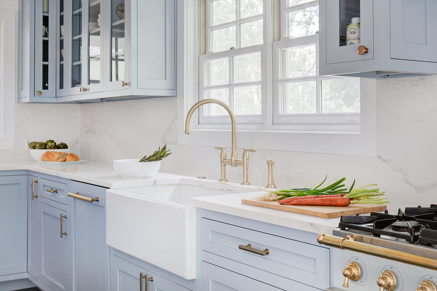 Shaw's original farmhouse white apron sink with gold faucet in a blue inset kitchen, gold hardware.